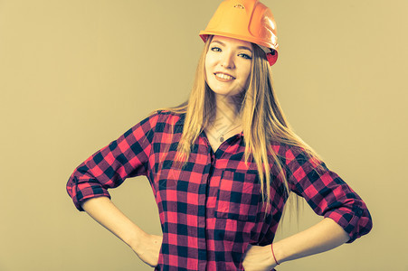 工业的一个年轻有魅力的女人肖像她金发碧眼戴着橙色头盔穿中灰色背景的格子衬衫金发女郎工人图片