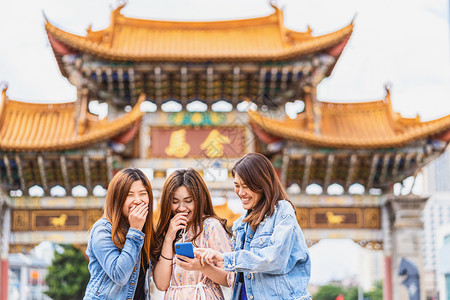 妇女在电话信息金碧快乐的在昆明金比广场昆明旅游与友谊概念上行时3个亚洲幸福妇女一起欢笑并使用智能手机进行社交网络的游戏活动c背景