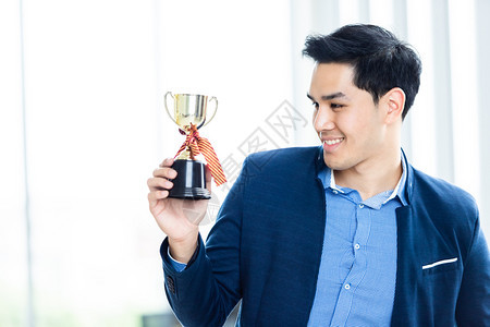 人们仪式成功感觉的胜利者肖像尖叫着英俊的年轻亚洲商人在办公室背景中拿着冠军杯在办公室背景行政人员图片