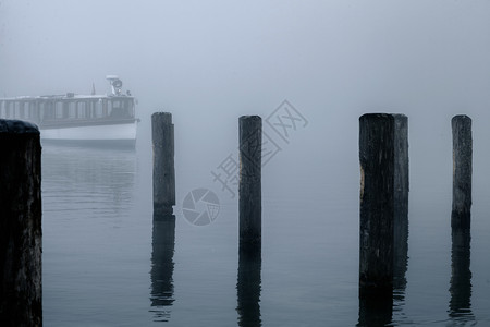 西湖冬天宁静反射德国科尼格西湖的雾中木头码和单船与在雾中失落的木桩上瓶子谷背景
