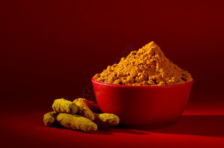 红色背景中碗的干姜黄粉和根或树皮哈里德拉油脂测量图片