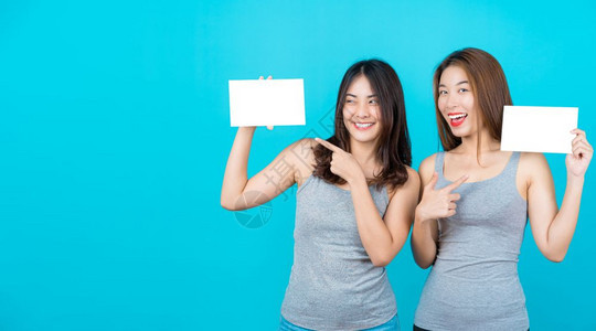 女士惊人的颜色两个笑亚洲青年妇女展示和关于孤立蓝色背景的海报在夏季室内工作穿防弹衣小册子和白广告纸等夏季室内工作图片