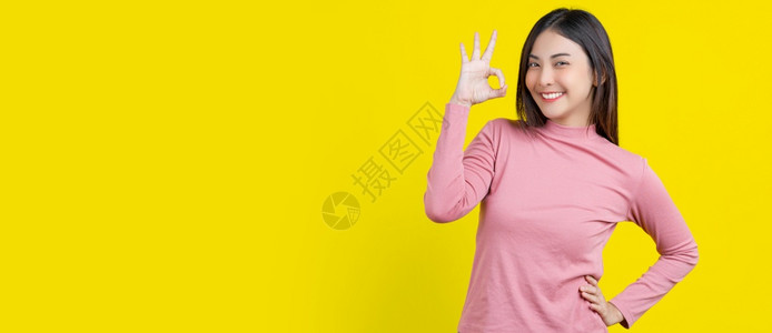 机械工业bannerBanner微笑着的亚洲年轻女子在等待批准或就孤立黄色背景签署协议的好名穿着冬季舒适的衣室内工作幸福和乐观的决定复制空间等事项上背景