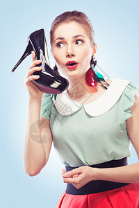 谣言吸引人的坦率像电话一样用鞋贴近脸部说话蓝背景的Pinup风格年轻惊艳女人图片