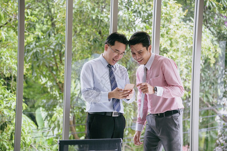 工人胜利男成功的实业家从手机智能上得到好消息商业界如此成功的亚洲青年商人在接到电话大新闻后快乐地举起手来笑着微图片