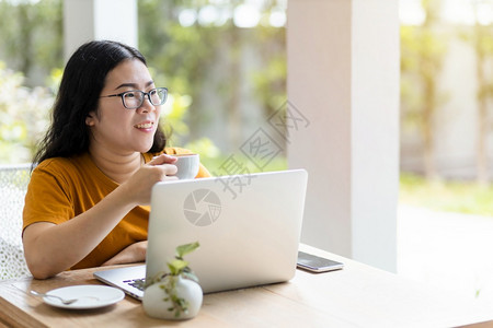 杯子女在咖啡店用笔记本电脑工作并像背景沟通概念一样在咖啡店里持有和智能手机校对Portnoy幸福数字的图片