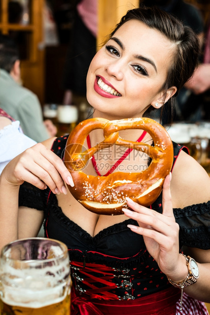 在传统Dirndl饮食OktoberfestPretzel和喝酒啤多种族亚洲菲律宾以及高加索混合中有吸引力的年轻女高德纳快乐椒盐图片