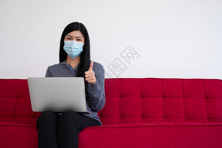 戴口罩在沙发上用笔记本电脑在家工作的女性图片