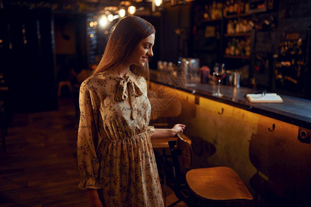 庆典一个年轻的女人带着一杯红酒坐在吧的柜台上一个女人在酒吧里类的情感休闲活动一个带着红酒的女人坐在吧里红色的裙子图片