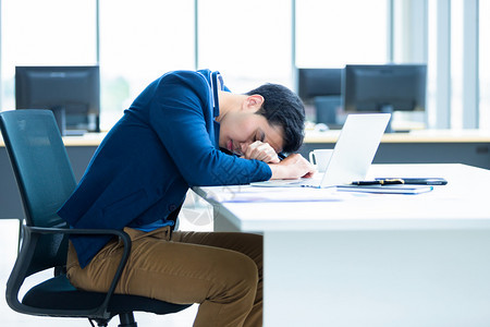 亚洲青年商人工作到很晚在笔记本电脑上睡着位于办公室背景中白种人金融挫折图片