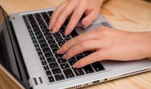 数字的公司个人电脑使用灰色笔记本电脑并在黑键盘上打字的年轻女士双手在一间房内打字办公室用品技术装置和木制办公桌图片
