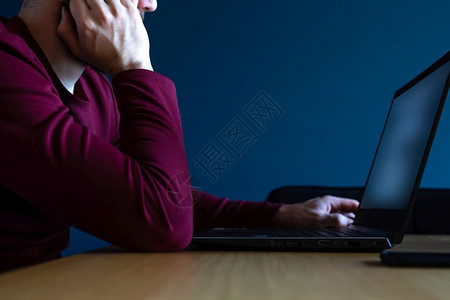 在室内冲浪年轻人在深夜用蓝色背景的笔记本电脑上网用喜怒无常的蓝色和红深夜工作年轻人在深夜用蓝色背景的笔记本电脑上网用喜怒无常的蓝图片