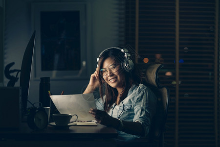 商业成功亚洲女人的肖像她坐在桌上辛勤地工作与幸福行动晚些时在工作场所计算机桌面前摆着电脑努力工作与为时太晚的概念集中注意力图片