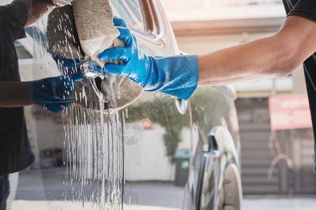 污垢洗车工作人员戴蓝色橡胶手套使用加肥皂和水的湿润海绵清洗汽车库闪亮的图片