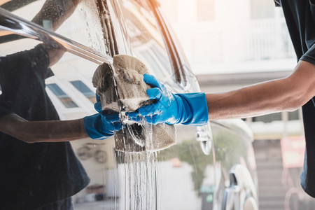 污垢闪耀洗车工作人员戴蓝色橡胶手套使用加肥皂和水的湿润海绵清洗汽车商业图片