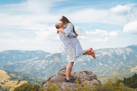 年轻夫妇在山顶岩石上穿白色衣服男人抱着他女朋友老婆未婚妻拥抱和