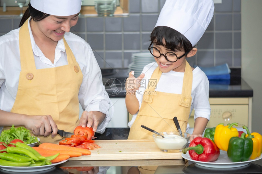 亚洲年轻母亲有儿子和的亚洲女年轻母亲烹饪沙拉食物配菜端着番茄和胡萝卜盘子里放铃椒供幸福家庭煮饭时用在家做享受生活方式厨师微笑童年图片