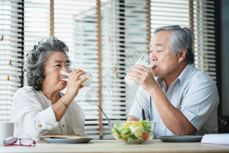 人们蛋白质坐在桌边喝着牛奶杯互相看着彼此幸福的老年夫妇在家中吃早餐的同时享受健康沙拉食物并微笑着的亚洲老人男女笑声肖像图片