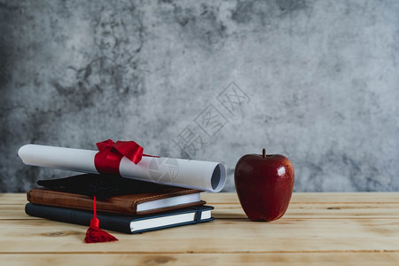 近距离毕业教育季节背景概念附属帽配有证书纸本和红苹果上面是现代生锈棕褐木和大学灰色水泥研究生的红苹果礼物文凭优质的图片