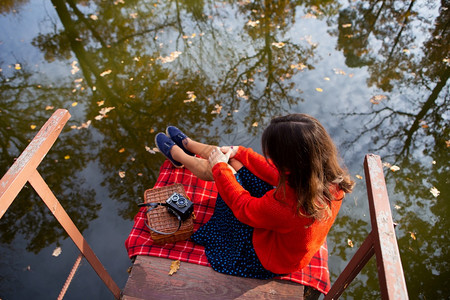 温暖的景观一位年轻女士坐在湖边的桥上一个阳光明媚的天个温暖和美丽的秋天普莱德毯子老相机一个年轻女士与她的背坐在一起湖边的个桥上阳图片