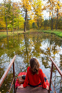 看头发肖像一个年轻女子背坐在湖边的桥上阳光明媚的日子里温暖美丽的秋天格子毯老相机图片
