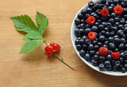 摄影肉类开胃绿色的叶子和小红莓躺在一块满是蓝莓和草的盘子旁边一块旧木头表面上有一片绿莓和浆果背景图片