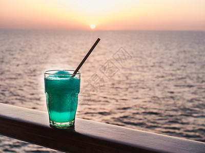 薄荷船绿色美丽的玻璃明亮鸡尾酒有冰和稻草在海浪日落的背景下站在露天甲板上侧面观海浪和夕阳背景紧贴的休闲和旅行概念美丽的玻璃和用冰图片