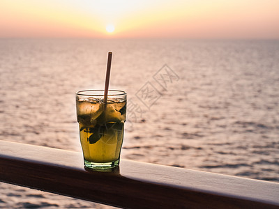 凉爽的游艇美丽玻璃明亮鸡尾酒有冰和稻草在海浪日落的背景下站在露天甲板上侧面观海浪和夕阳背景紧贴的休闲和旅行概念美丽的玻璃和用冰开图片