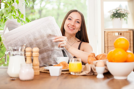 一种女士微笑Caucasian褐色女人在家吃早饭时看报纸的照片图片