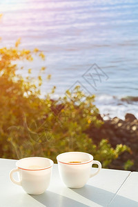 晴天夏在阳台上喝两杯咖啡可以看到大海和岸边的树木阳光明媚的早晨背景柔和焦点阳台上的两杯咖啡可以看到海岸上的洋和树木阳光美丽的早晨图片