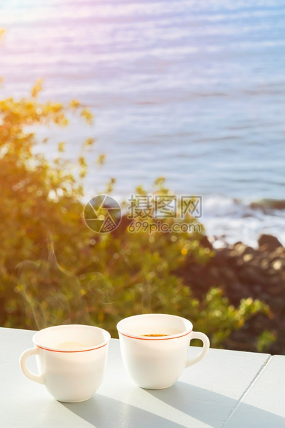 晴天夏在阳台上喝两杯咖啡可以看到大海和岸边的树木阳光明媚的早晨背景柔和焦点阳台上的两杯咖啡可以看到海岸上的洋和树木阳光美丽的早晨图片