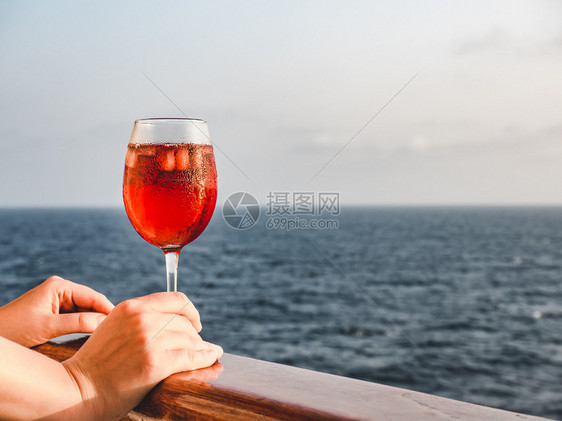 游艇白色的栏杆在蓝海浪的背景下在游轮的露天甲板上拿着一杯漂亮的粉红葡萄酒时尚女人侧视图特写休闲和旅行的概念女人拿着一杯漂亮的葡萄图片