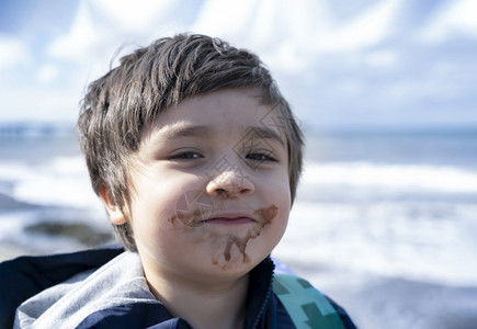 基德头被射中孩子用脏嘴吃巧克力冰淇淋和模糊的海景背康迪拍摄了快乐的孩子独自站着看镜头带微笑的脸看摄影机一个男孩在夏天户外玩耍相机图片