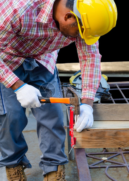 男木匠用锤子把钉在木板上的工具和制程概念设备红色的头盔安全图片