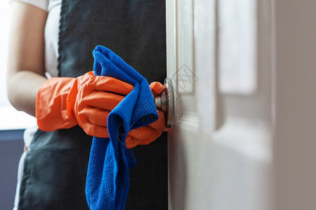 旋钮妇女手拿橙色橡胶套在门面触摸时打扫门把手用蓝色清洁布和对CoronaCOVID19预防概念的感染家政庭图片