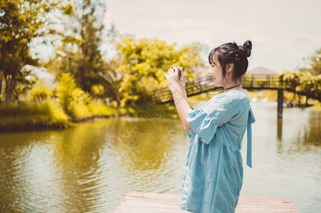 假期学习公园里身穿蓝色连衣裙的亚洲女手持数码无反光镜相机不戴口罩拍照心情愉快人们的生活方式和休闲概念户外旅行和自然主题摄影师图片