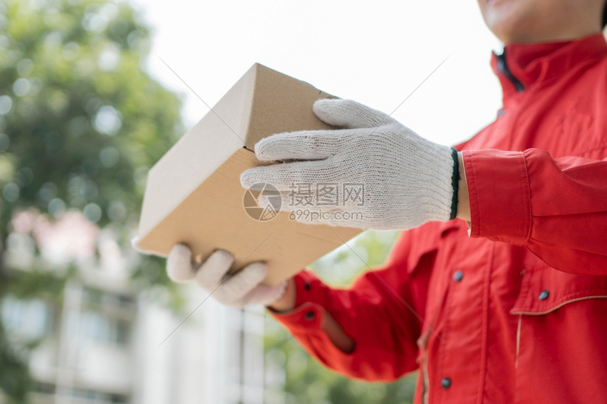Covid19大流行期间一些后勤公司将包裹交给客户的邮递员身着红色制服和手套的邮递员在Covid19大流行期间将包裹交给客户抓住图片