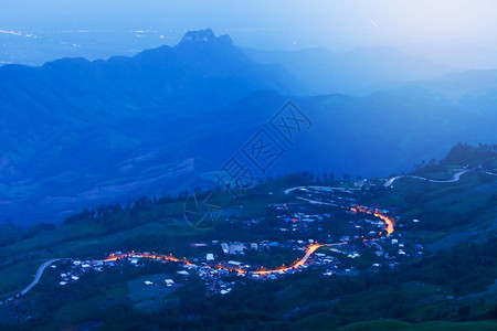 黄昏暮森林对日落时山路的触目惊艳弯曲沥青路与灯光从前处发的沥青路经过蓝色山脉泰国PhuThapBoek长期点集中在公路上图片