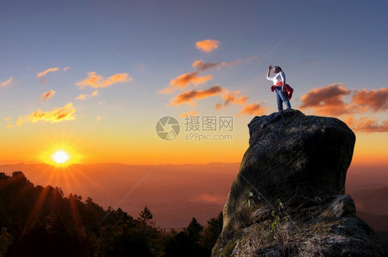 亚洲女登山者或背包站立透过日落时岩石峰顶的高树仰望着亚洲女登山者或背负式妇女极好的勇气攀登图片