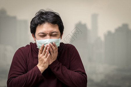 高公寓阳台上咳嗽可以看到Bangkok市风背景的污染和浓雾保健概念在高楼露台时亚洲男子戴着面罩防止空气污染在高楼阳台上咳嗽这可以图片