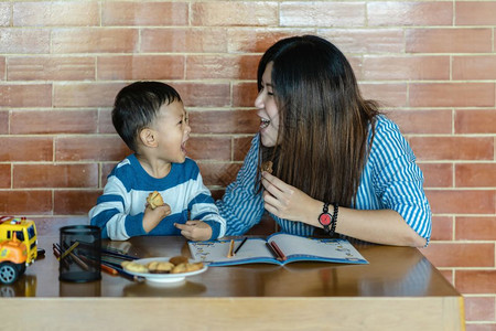 男生有儿子的亚洲单身母亲一起画和吃饼干住在自学或家庭校的阁楼家庭和单亲妈概念选择重点等有的家里与儿子同在的亚洲单身母亲一起绘画并图片