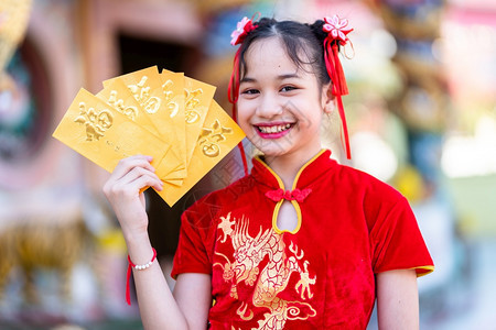 可爱的节日身着红色传统长相装饰的可爱亚洲小女孩手拿着黄信封准备在神庙举办新年庆典她戴着黄包美丽的图片