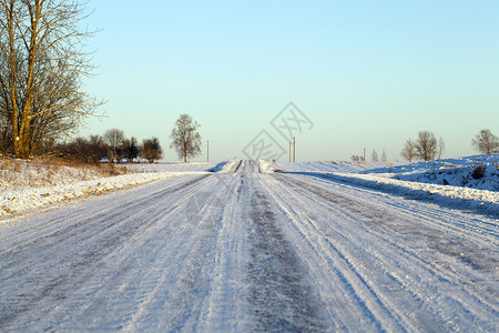 在雪堤表面经过的汽车痕迹可见于积雪公路背景轨迹中的森林和蓝天空在积雪路面上通过车辆的痕迹可见森林和蓝色天空户外寒冷的若冰霜图片