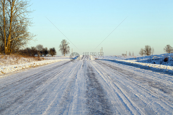 在雪堤表面经过的汽车痕迹可见于积雪公路背景轨迹中的森林和蓝天空在积雪路面上通过车辆的痕迹可见森林和蓝色天空户外寒冷的若冰霜图片