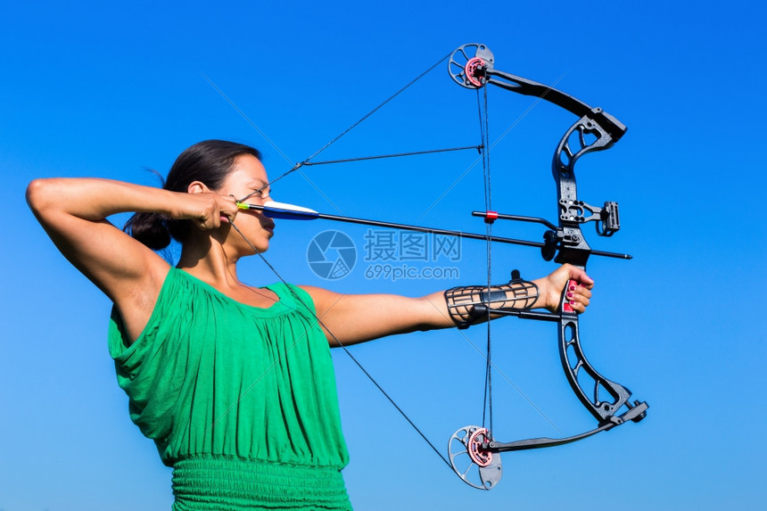 专业知识获得年轻的黑发女青向蓝天的复合弓箭瞄准罗宾图片