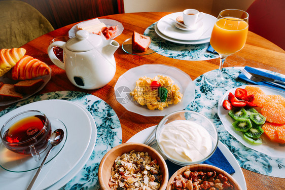 食物早餐桌包括谷类食品酸奶炒鸡蛋水果羊角面包和茶咖啡橙汁等饮料早餐桌包括谷类食品羊角面包和茶等饮料咖啡和橙汁烹饪有机的图片