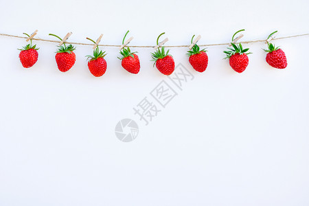 夏天红色成熟草莓的花环挂在绳索上的木衣夹位于白色木材背景的顶部边缘复制空间文本设计明信片或邀请的创意模板红色成熟草莓的花环挂在绳图片