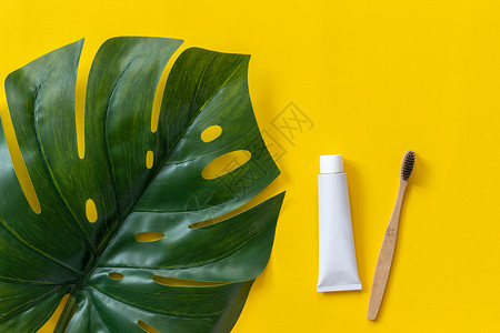 天然环保竹刷牙膏管和热带叶龟背竹套装用于在纸黄色背景上洗涤顶视图平躺工艺浴室治疗图片