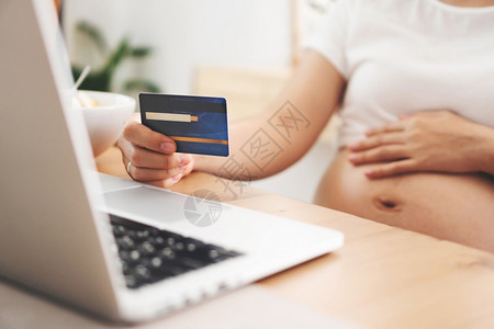 数字的母蓝色持有信用卡并在家中电脑上用笔记本在线付费购物的孕妇在互联网银行进采购的妇女花钱和生活方式以支付金钱和生活方式为目的第图片