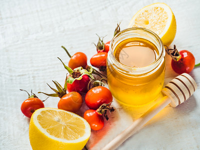白木板上的新鲜黄柠檬一壶蜂蜜和红浆果风景近视孤立的防冷新黄色柠檬一壶蜂蜜和红莓子概念防止流感玻璃图片